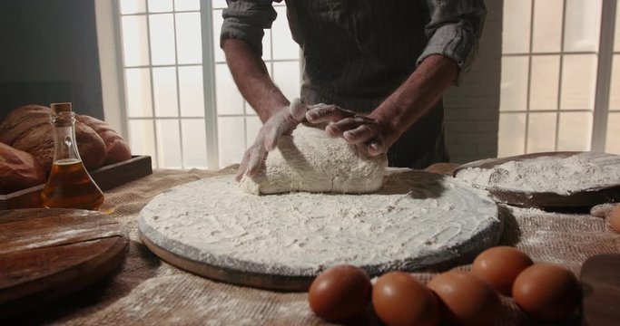Closeup shot of hands of mature chef working in bakery shop applying flour and kneading dough for bread with his traditional techniques and recipe 4k footage