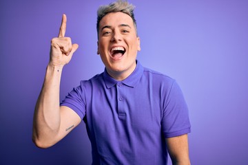Fototapeta premium Young handsome modern man wearing casual purple t-shirt over isolated background pointing finger up with successful idea. Exited and happy. Number one.