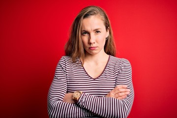 Young beautiful blonde woman wearing casual striped t-shirt over isolated red background skeptic...