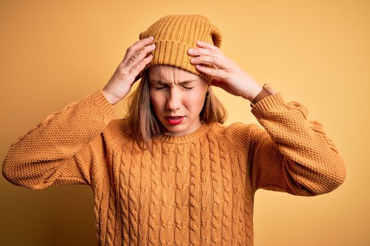 Young beautiful blonde woman wearing casual sweater and wool cap over yellow background suffering from headache desperate and stressed because pain and migraine. Hands on head.