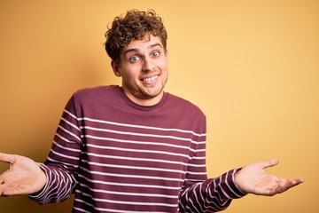 Young blond handsome man with curly hair wearing casual striped sweater clueless and confused...