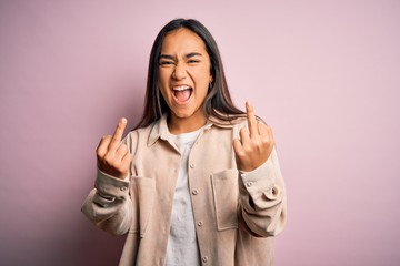 Naklejka premium Young beautiful asian woman wearing casual shirt standing over pink background Showing middle finger doing fuck you bad expression, provocation and rude attitude. Screaming excited