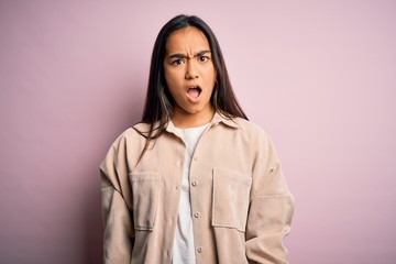 Young beautiful asian woman wearing casual shirt standing over pink background In shock face,...