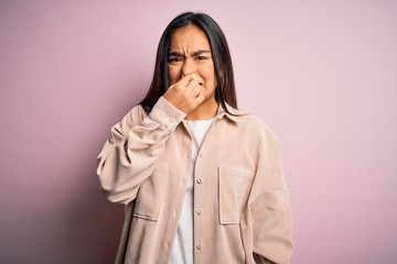 Young beautiful asian woman wearing casual shirt standing over pink background smelling something...