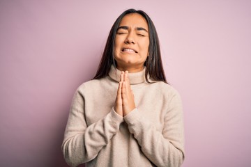 Young beautiful asian woman wearing casual turtleneck sweater over pink background begging and...