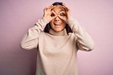 Fototapeta premium Young beautiful asian woman wearing casual turtleneck sweater over pink background doing ok gesture like binoculars sticking tongue out, eyes looking through fingers. Crazy expression.