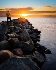 Beautiful calm sunrise over the Baltic sea with old rocky pier in foreground with a man standing on...