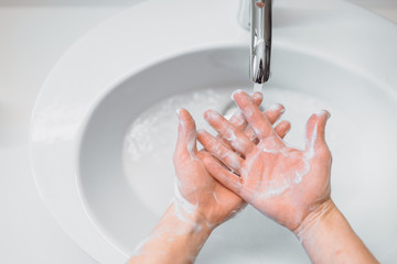 caucasian woman carefully washing hands with soap and sanitiser in home bathroom. top view, details of hygiene