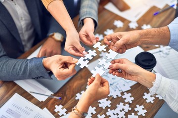 Group of business workers with hands together connecting pieces of puzzle at the office