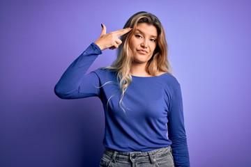 Young beautiful blonde woman wearing casual t-shirt over isolated purple background Shooting and killing oneself pointing hand and fingers to head like gun, suicide gesture.