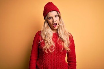 Young beautiful blonde woman wearing casual sweater and wool cap over white background In shock face, looking skeptical and sarcastic, surprised with open mouth