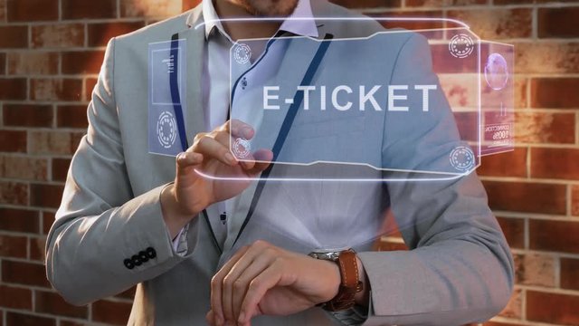 Unrecognizable businessman activates conceptual HUD holograms on smartwatch with text E-ticket. Man in jacket with holographic technology on wristwatch on background of brick wall