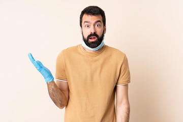 Caucasian man with beard protecting from the coronavirus with a mask and gloves over isolated background making doubts gesture