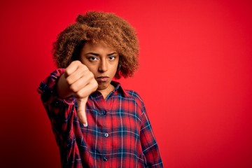 Young beautiful African American afro woman with curly hair wearing casual shirt looking unhappy and angry showing rejection and negative with thumbs down gesture. Bad expression.