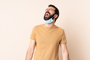 Caucasian man with beard protecting from the coronavirus with a mask and gloves over isolated background laughing
