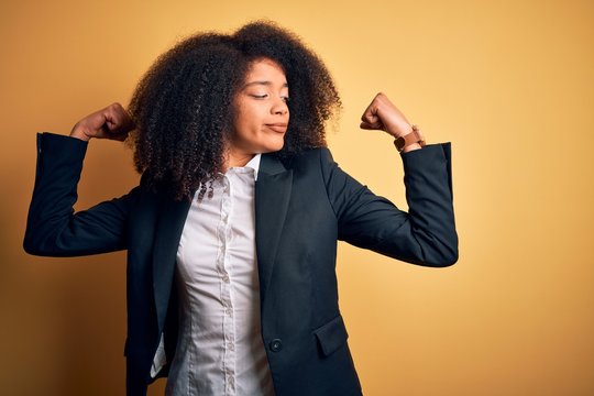 Young beautiful african american business woman with afro hair wearing elegant jacket showing arms muscles smiling proud. Fitness concept.