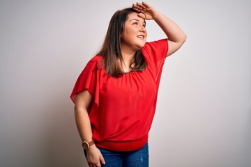 Beautiful brunette plus size woman wearing casual red t-shirt over isolated white background very happy and smiling looking far away with hand over head. Searching concept.