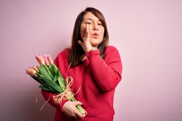 Beautiful plus size woman holding romantic bouquet of natural tulips flowers over pink background hand on mouth telling secret rumor, whispering malicious talk conversation