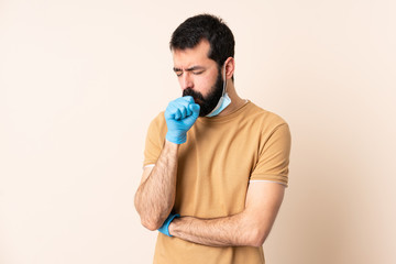 Caucasian man with beard protecting from the coronavirus with a mask and gloves over isolated background coughing a lot