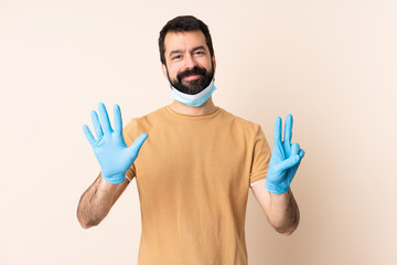 Caucasian man with beard protecting from the coronavirus with a mask and gloves over isolated background counting seven with fingers