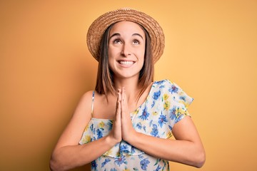 Young beautiful woman wearing casual t-shirt and summer hat over isolated yellow background begging and praying with hands together with hope expression on face very emotional and worried. Begging.