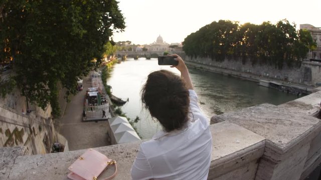 Young woman taking pictures from a bridge on river tiber in Rome. View of St. Peter and Vatican city, Italy.