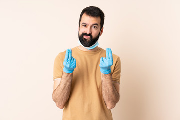 Fototapeta premium Caucasian man with beard protecting from the coronavirus with a mask and gloves over isolated background making money gesture but is ruined
