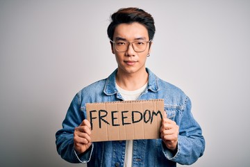 Young handsome chinese activist man protesting asking for freedom holding poster with a confident expression on smart face thinking serious