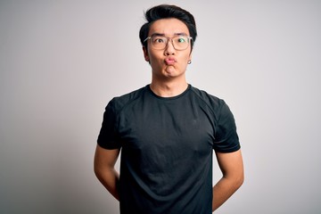 Young handsome chinese man wearing black t-shirt and glasses over white background making fish face with lips, crazy and comical gesture. Funny expression.