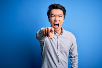 Young handsome chinese man wearing casual shirt standing over isolated blue background pointing displeased and frustrated to the camera, angry and furious with you