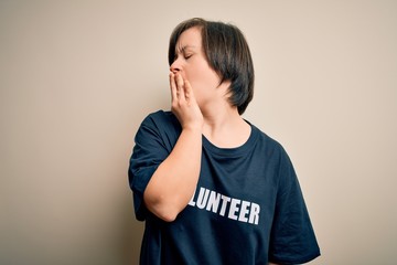 Young down syndrome volunteer woman wearing social care charity t-shirt bored yawning tired...