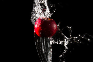 The water splashes the apple on the water until it spreads beautifully on a black background.