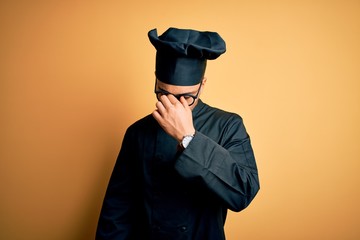 Young brazilian chef man wearing cooker uniform and hat over isolated yellow background tired rubbing nose and eyes feeling fatigue and headache. Stress and frustration concept.