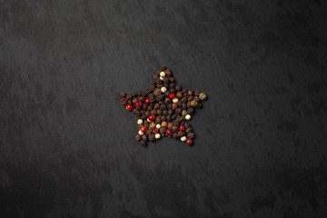 Peppercorn pepper on a black background, laid out in the shape of a star. Red, white, green and black peppers. peas pepper. black slate background