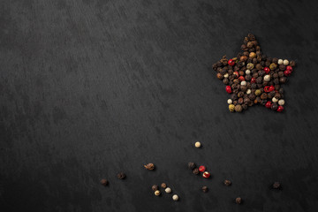 Peppercorn pepper on a black background, laid out in the shape of a star. Red, white, green and black peppers. peas pepper. black slate background