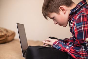 boy in plaid shirt does lessons on laptop. child learns remotely during quarantine of coronavirus. Online learning from home.