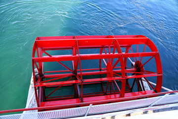 A bright red paddle wheel from a boat on a lake