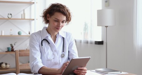 Happy female professional doctor using digital tablet in hospital. Smiling young woman physician holding modern tech pad device working in medical office. Healthcare technology and medicine concept - Powered by Adobe