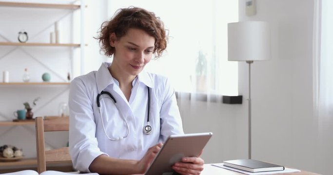 Happy female professional doctor using digital tablet in hospital. Smiling young woman physician holding modern tech pad device working in medical office. Healthcare technology and medicine concept