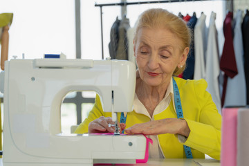 female senior dressmaker using sewing machine making dress at fashion design shop