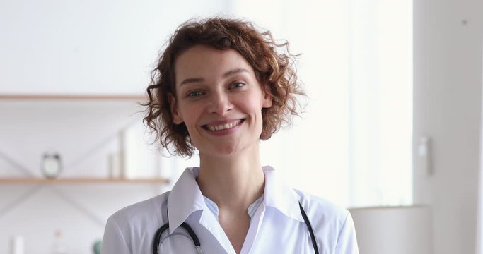 Happy young european woman doctor wearing white medical coat and stethoscope looking at camera. Smiling female physician posing in hospital office. Positive general practitioner close up face portrait