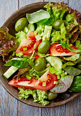 Healthy salad with green olives, cucumber and tomatoes. Rustic wooden background. Top view. Close up. 
