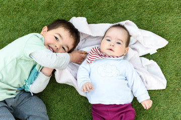 Hermanos felices tumbados sobre cesped verde