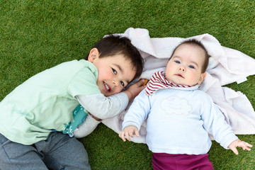 Hermanos felices tumbados sobre cesped verde