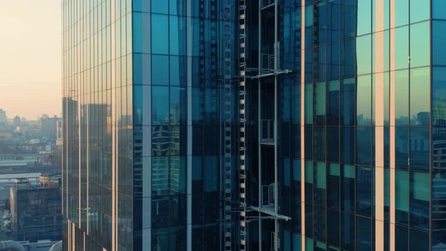 Aerial elevator shot of glassed skyscraper exterior with a reflection of the cityscape in the windows at sunset