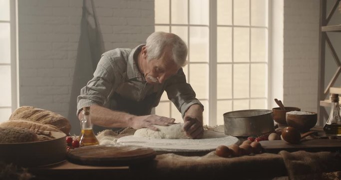 Retired senior moustached caucasiam man is making a loaf of bread, enjoying his hobby after retirement. Professional experienced baker working in bakery shop 4k footage