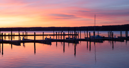 Fototapeta na wymiar Dock with Colorful Sunrise Sky of Pink and Orange on a Calm Tree Lined River at a Marina