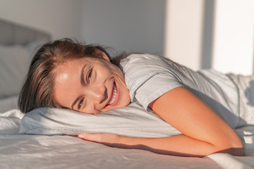 Fototapeta premium Happy home relaxation asian smiling woman staying in bed relaxing in bedroom candid portrait. Natural beauty healthy skincare model face. Comfortable foam mattress and pillow.