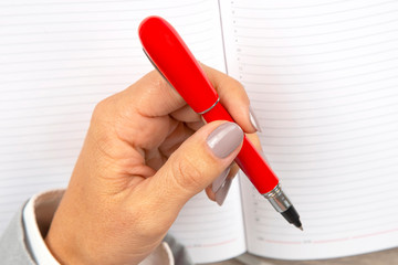 hand of a business woman is holding a red pen on a background of a notebook.