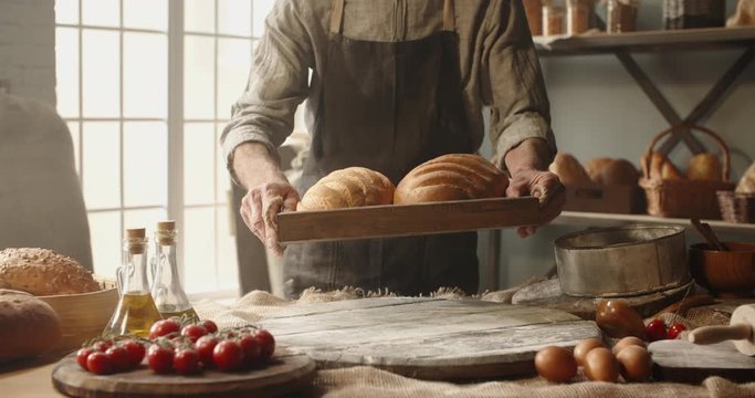 Positive elderly professional caucasian baker bringing fresh bread loafs basket, looking at camera and smiling. Retiree enjoying his new hobby portrait shot 4k footage